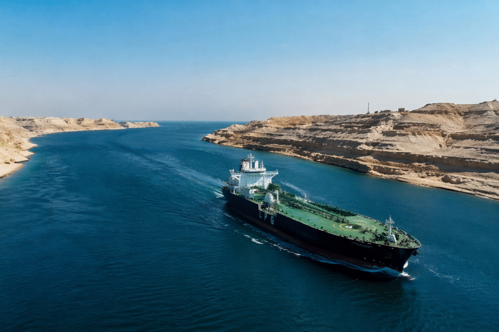 Daytime view of the Strait of Hormuz with a large cargo ship passing through blue water between rocky coastlines
