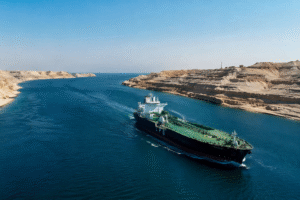 Daytime view of the Strait of Hormuz with a large cargo ship passing through blue water between rocky coastlines